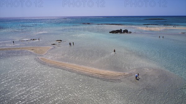 Sandbank in clear, calm sea with scattered people enjoying the natural surroundings, Elafonissi,