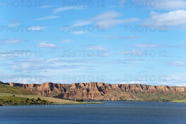 A clear blue lake surrounded by majestic rock formations and rolling hills under an expansive sky,