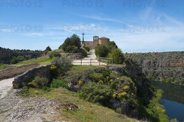 A picturesque church stands on a lush hill with a path, under a bright blue sky in a vast