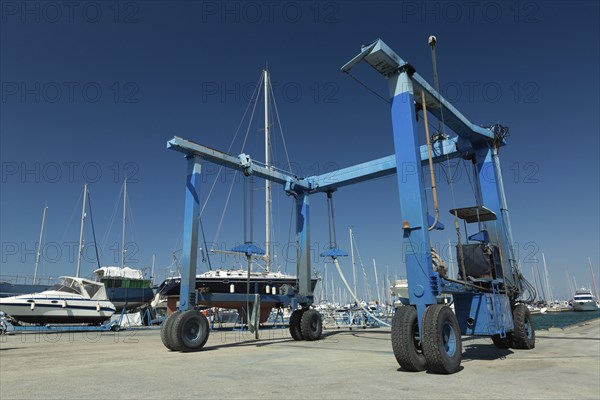 Blue lifting crane for elevating boat and maintenance machine at harbor dock