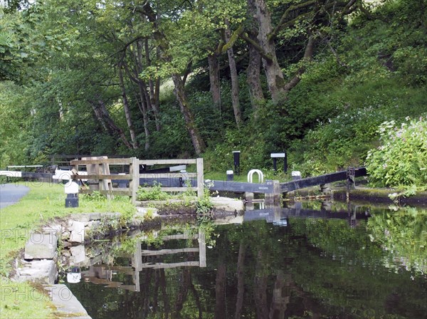 Old wooden lock gates with trees and flowers reflected in the water with mooring posts and fences
