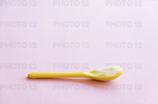 Spoon with sugar close-up on a pink background