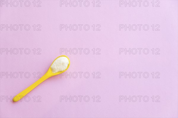 Spoon with sugar close-up on a pink background
