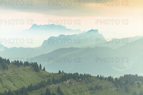 An impressive panorama of mountains with rocky peaks and dense forests under a cloudy sunset,