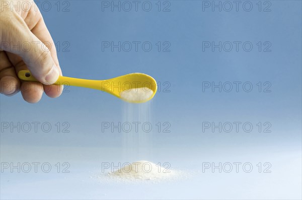 Yellow spoon turning sugar on blue background