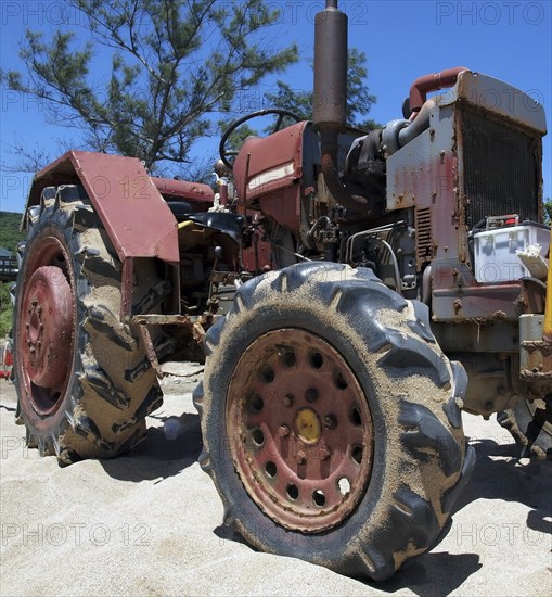 A rusting and corroded old tractor is parked on a sand beach