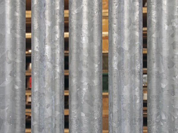 A close up of vertical galvanized steel fence with wooden pallets in outdoor storage visible
