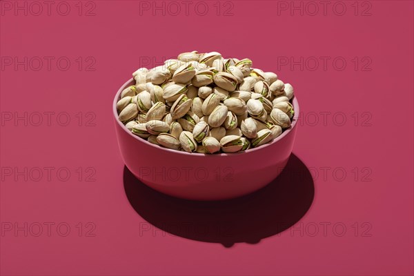 Pink bowl with roasted and salted pistachio minimalist on a magenta table. Bowl with pistachio