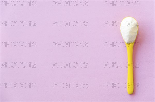 Spoon with sugar close-up on a pink background