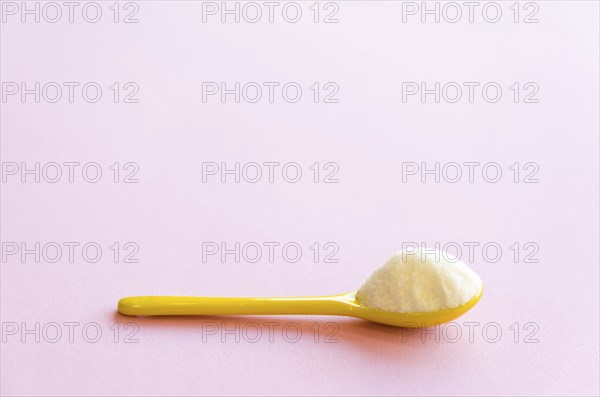 Spoon with sugar close-up on a pink background