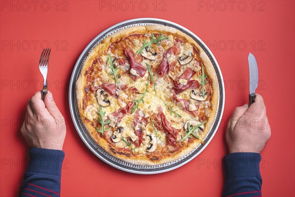 Man ready to eat a delicious homemade ham pizza. Top view with a prosciutto pizza on a red