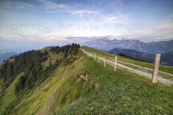 An impressive panorama of mountains with rocky peaks and dense forests under a cloudy sunset,