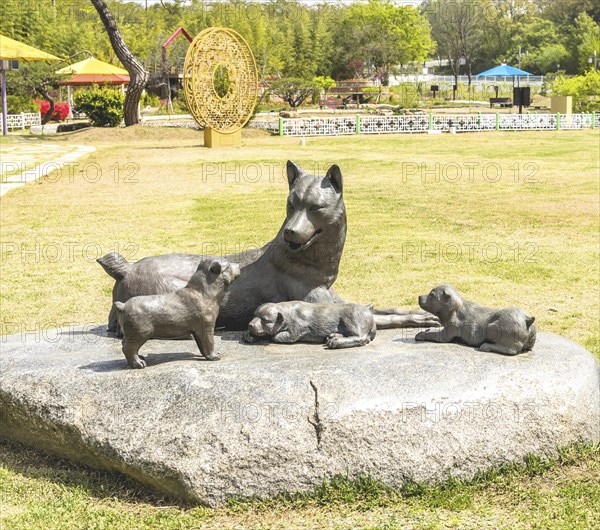 Sculpture of a dog with puppies in a green park, symbolizing family and nature, set in an outdoor
