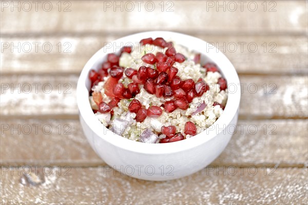 Quinoa salad with pomegranate seeds, radiccio, cucumber and olives on a light brown background