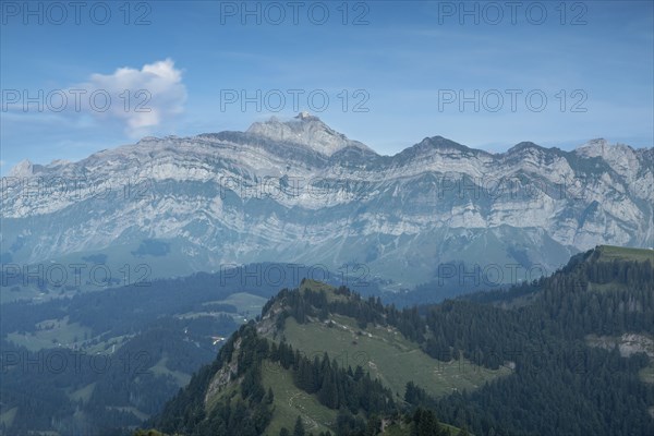 An impressive panorama of mountains with rocky peaks and dense forests under a cloudy sunset,