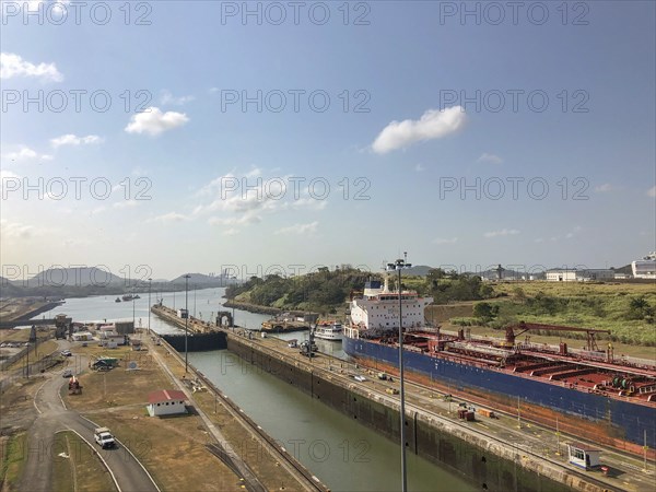 A tranquil canal scene with a large ship and buildings, the surrounding landscape is structured and
