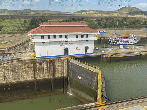 A picture of a lock with a large white building and a small boat. The surroundings are green and
