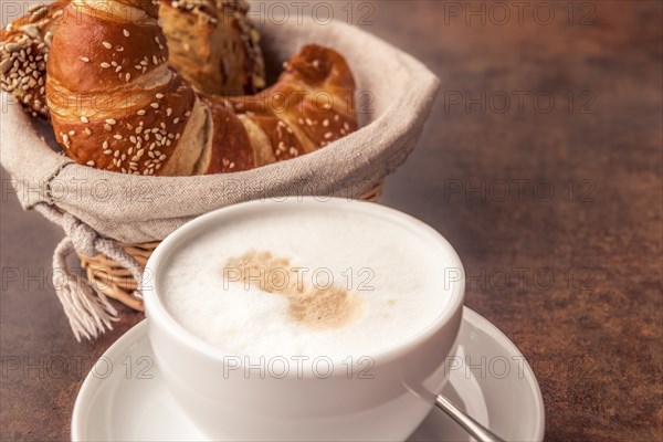 Delicious breakfast with a cup of milk coffee and fresh, sesame croissants in a rustic wicker