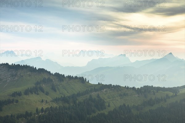 An impressive panorama of mountains with rocky peaks and dense forests under a cloudy sunset,