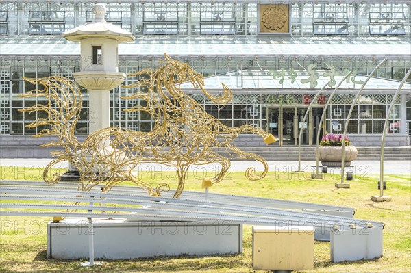 A golden sculpture of a horse next to a lantern in front of a building with a glass facade in