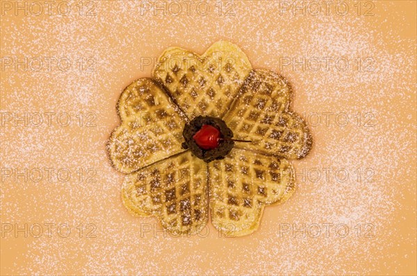 Homemade waffles with powdered sugar, a scoop of vanilla ice cream and a cherry on a pink