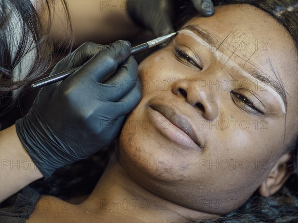 A person is lying down while having their eyebrows shaped using a makeup brush