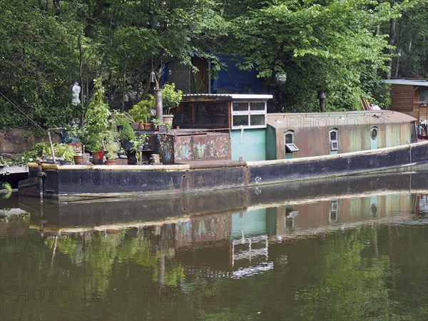 An old rusty narrow boat reflected in the water and surrounded by trees on the rochdale canal in