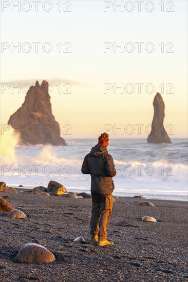 A tourist man with his back turned on the black sand beach of Reynisfjara at sunset in Iceland