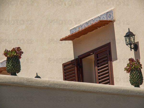 Open window with red shutters, potted plants and wall lamp on a beige wall, palermo, sicily,