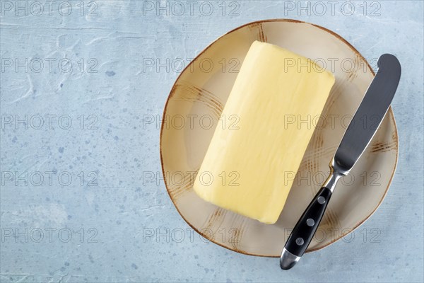 A block of butter with a knife on a plate, shot from above with a place for text