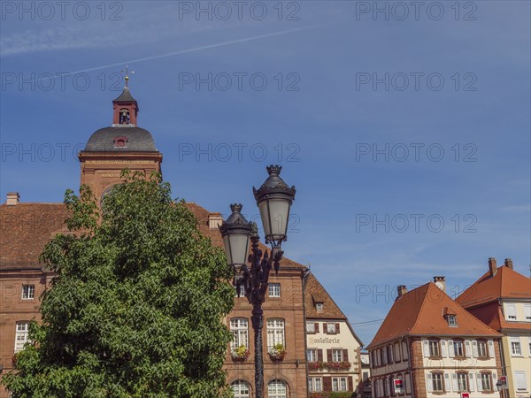 Historic buildings with red tiled roofs next to lanterns and trees under a clear sky, Weissenburg,