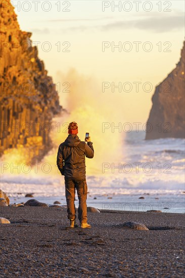 A tourist man taking a photo on the black sand beach of Reynisfjara at sunset in Iceland