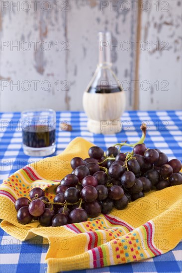 Bunch of red grapes and a glass of red wine with a wine flask on background over a checkered