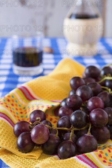 Closeup of a bunch of red grapes and a glass of red wine with a wine flask on background over a