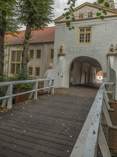 Wooden bridge and white archway in a historic building complex surrounded by autumn leaves and