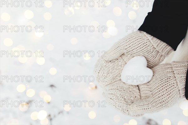 Snow heart snowball in girl gloved hands. Blurred background.