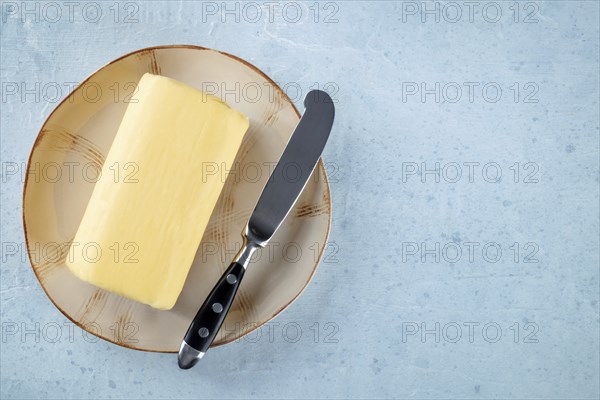 A block of butter with a knife on a plate, overhead flat lay shot on a light slate background, with