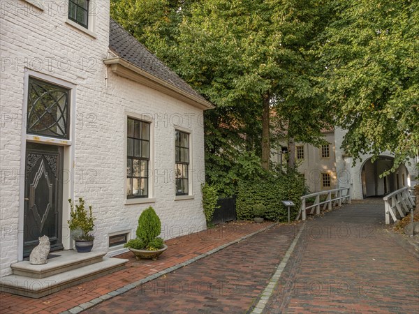 Plants and winding paths along a quiet lane with whitewashed buildings and a wooden bridge, dornum,