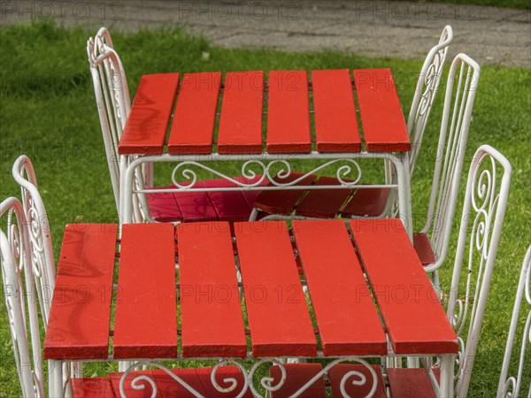 Two bright red garden tables with white metal chairs, decorated with artistic patterns, on a lush