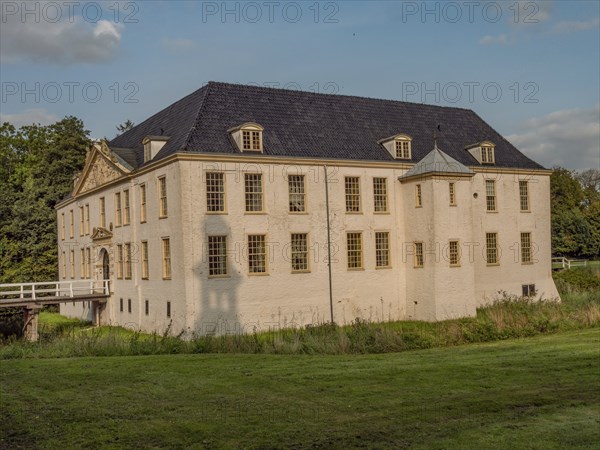 Historic castle with white walls and blue roof, nestled in a large green meadow under a blue sky,