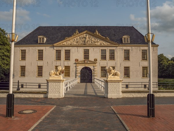 Elegant historic manor house with lion statues and flagpoles against a blue sky, dornum, east