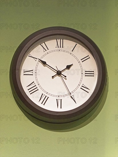 Big old clock with Roman numbers at green wall
