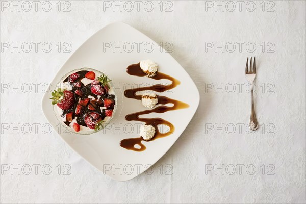 Dessert with strawberries and yogurt in a bowl over a square plate with decorations and cream seen
