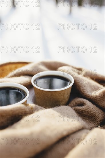 Two cups of coffee on a scarf in the snowy forest.
