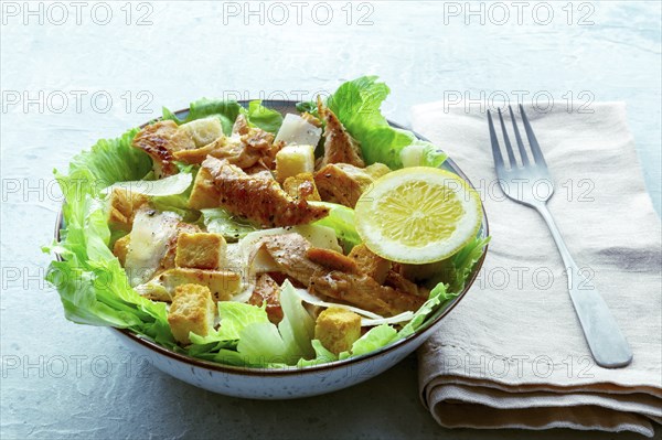 Caesar salad with chicken breast, lettuce, croutons, and a lemon, on a slate background, with a