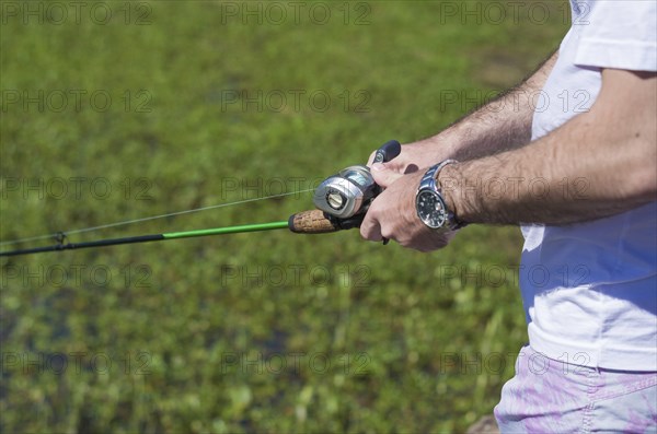 Young man fishing in pond, lake, closeup of fishing rod and reel