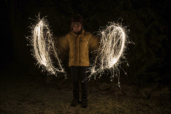 A child paints circles of light with sparklers