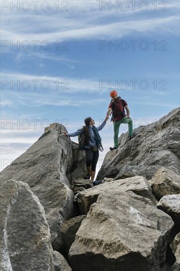 Male and female climbers high-fiving at the top of the mountain. Mixed rock climbing team