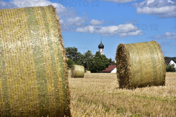 Straw bales on a harvested grain field, in the background the village church with onion tower,