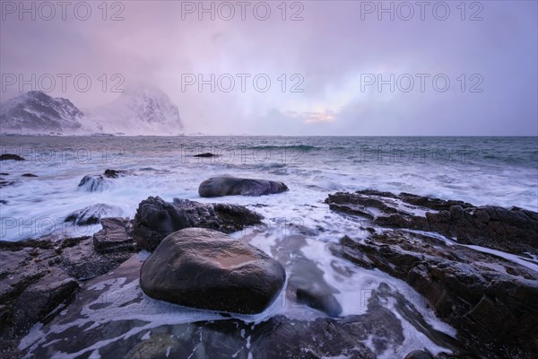 Beach of Norwegian sea on rocky coast in fjord on sunset in winter. Vareid beach, Lofoten islands,